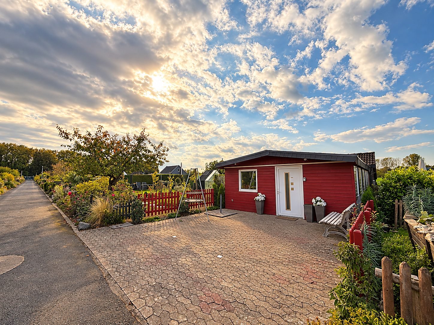 Das rote Vereinsheim mit weißer Tür und gepflastertem Vorplatz unter weitem Himmel mit Abendsonne